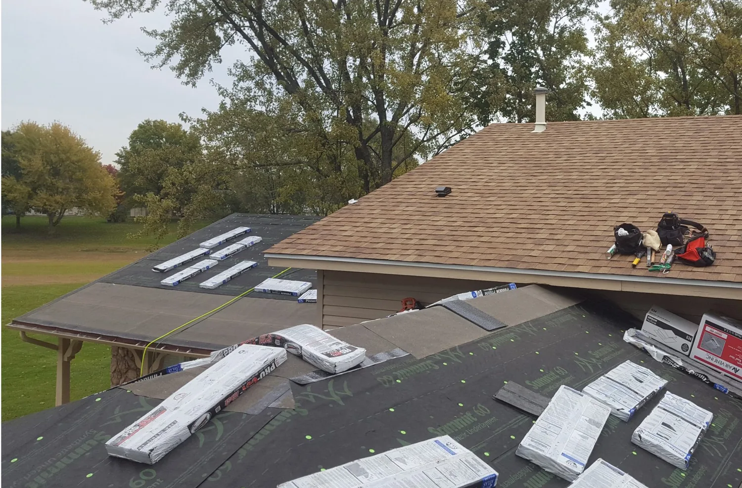 New shingles being installed over fresh underlayment on a suburban home, with bundles staged across the roof