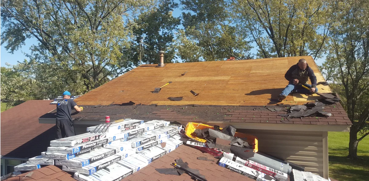 Two roofers stripping old shingles down to bare decking on a single-story home